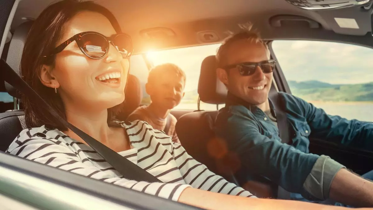 Eine Familie sitzt im Auto. Die Mutter schaut zu den Kindern. Sie hält eine Karte in der Hand.