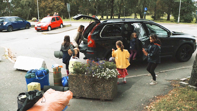 Eine Familie mit zwei Kindern packt das Auto für einen Ausflug. Die Mutter lädt das Auto auf.