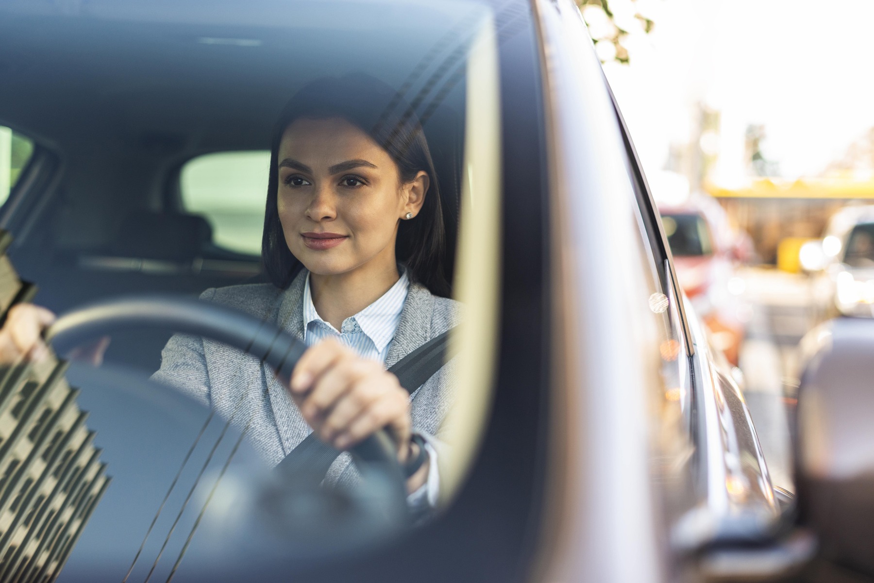 Eine Frau fährt in einem Auto. Das Auto hat helle Sitze. Die Frau hat blonde Haare.