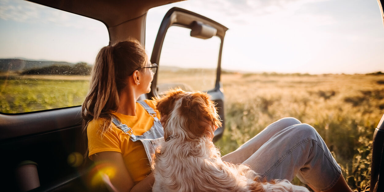 Eine Frau steht neben ihrem Auto mit dem Gesicht zur Landschaft gerichtet.